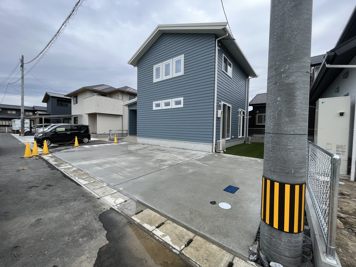 青い外壁に映える、広々とした駐車スペースと緑豊かな人工芝のお庭